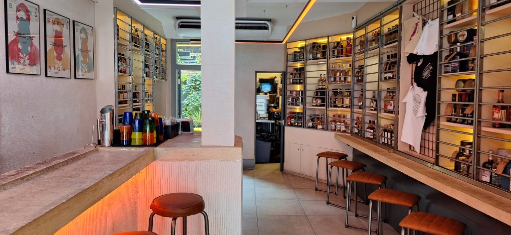 Interior of Dram Bar London during the day with bottles on display on the walls, the stone bar visible and no customers present