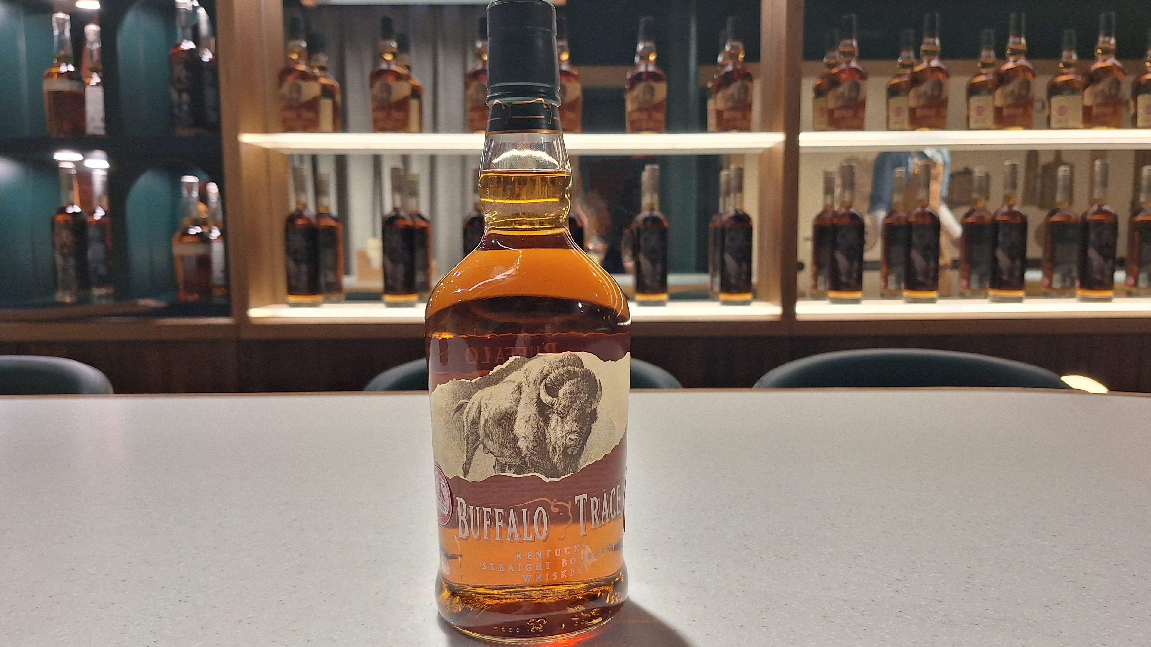A close up of a buffalo trace bottle showing the front image on a table with bottles behind